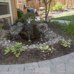 natural stone in landscape bubbler surrounded by plants and curved walkway