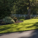 lawn and landscaping in front of white fence with tree