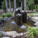 3 pillar stone water feature surrounded by water, plants and rock