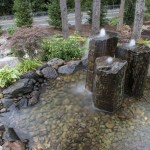 3 pillar stone water feature with rocks and plants surrounding