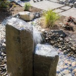 stone pillar water feature next to rocks and pavers