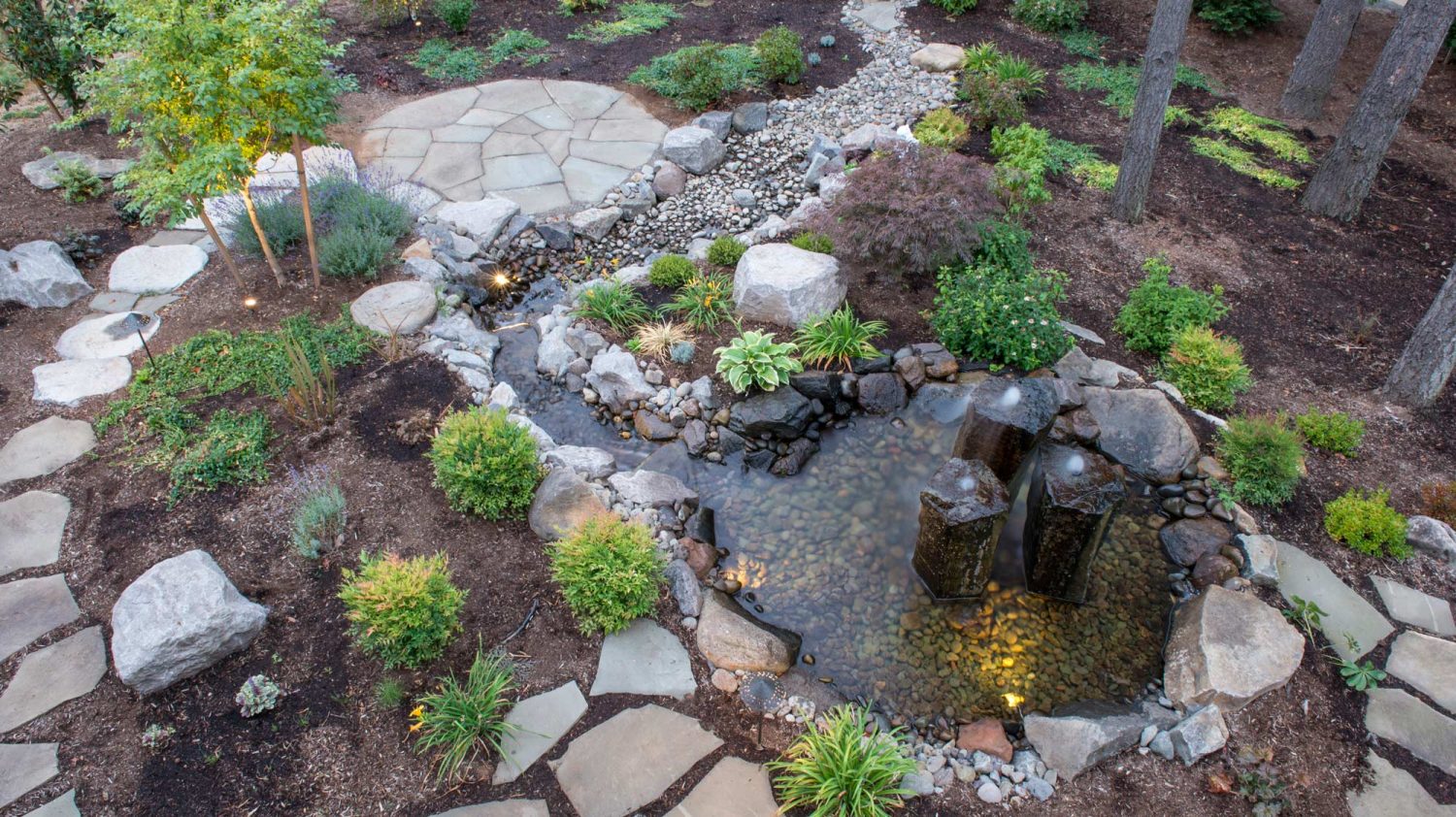 outdoor lighting of a fountain with plants and patio pavers